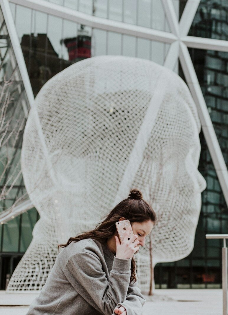 woman sitting on ground holding smartphone near building